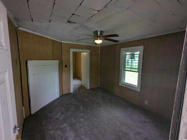 unfurnished bedroom with carpet floors, ornamental molding, wooden walls, and a ceiling fan