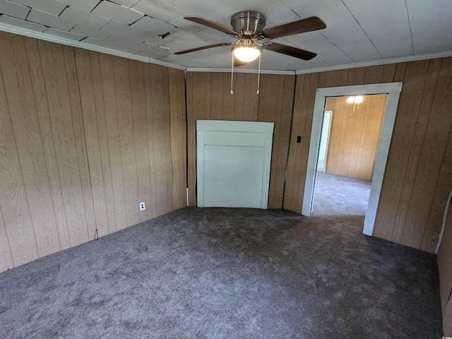 unfurnished room with a ceiling fan, dark colored carpet, crown molding, and wooden walls