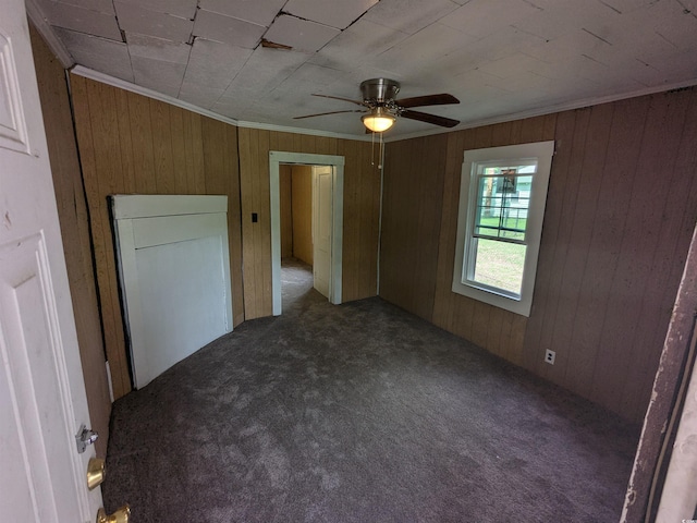 unfurnished bedroom featuring ornamental molding, dark carpet, wood walls, and ceiling fan