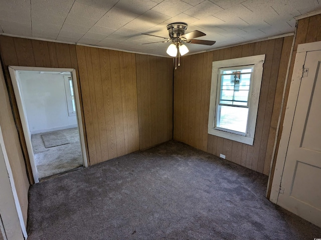 spare room featuring a ceiling fan, dark carpet, and wooden walls