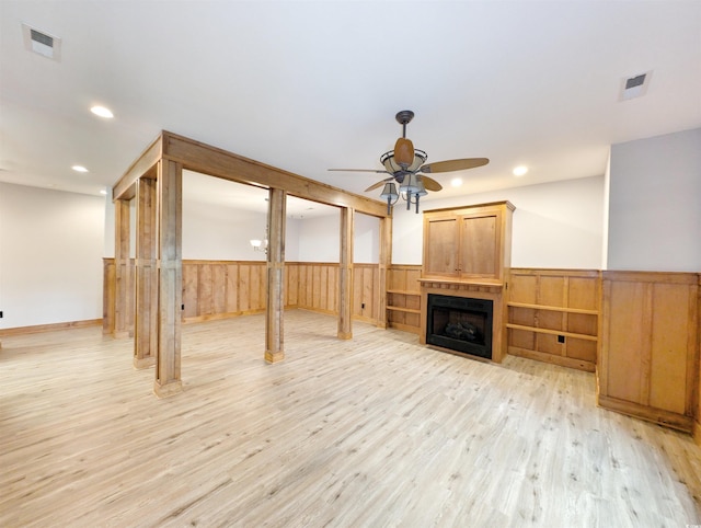 unfurnished living room featuring light hardwood / wood-style floors, wood walls, and ceiling fan