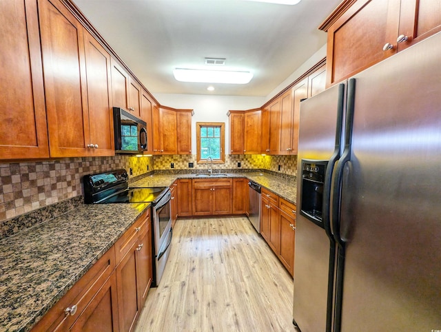kitchen with appliances with stainless steel finishes, dark stone counters, decorative backsplash, sink, and light hardwood / wood-style flooring