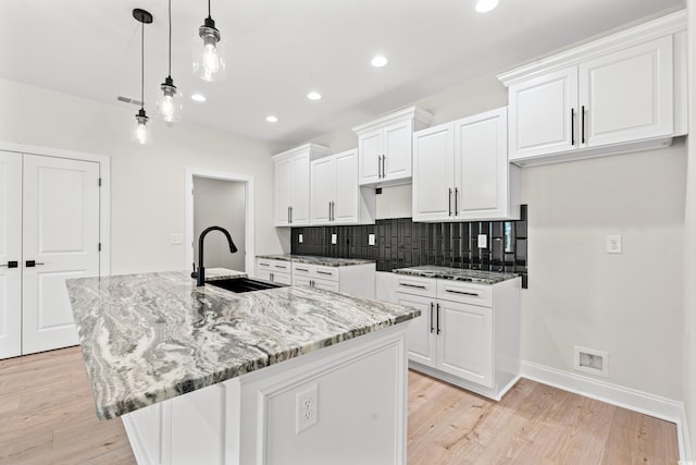 kitchen featuring a center island with sink, white cabinets, a sink, light wood-type flooring, and backsplash