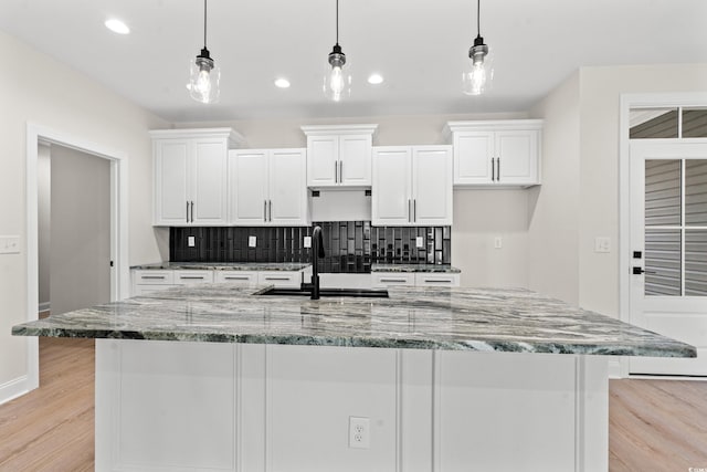 kitchen with light wood finished floors, tasteful backsplash, white cabinetry, a sink, and an island with sink