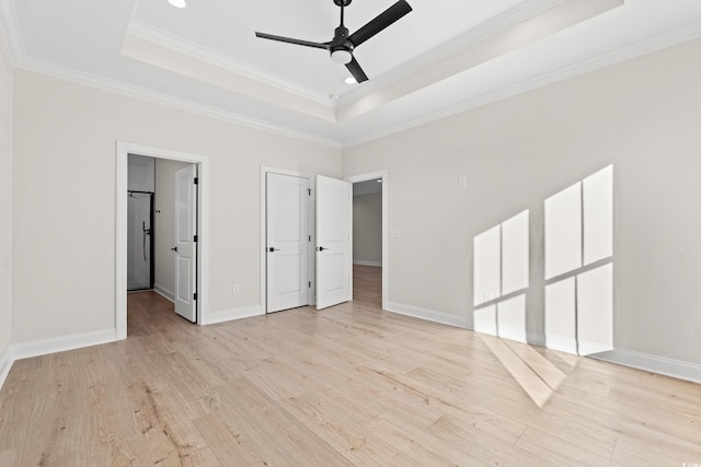 unfurnished bedroom with a tray ceiling, light wood-type flooring, stainless steel refrigerator, and baseboards