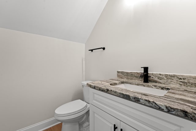 bathroom featuring toilet, wood finished floors, vanity, baseboards, and vaulted ceiling