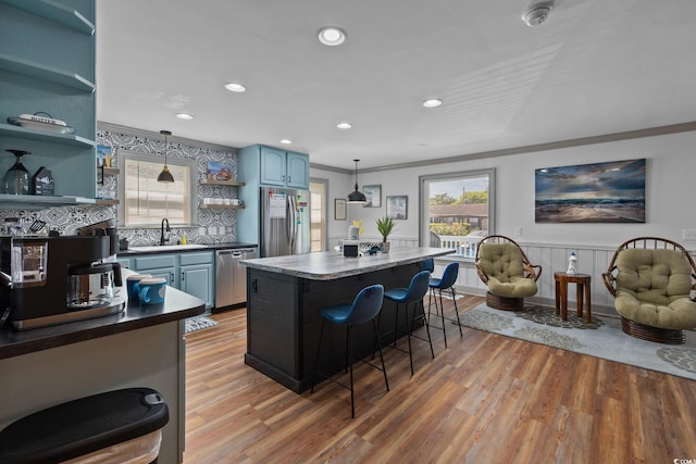 kitchen with blue cabinets, pendant lighting, stainless steel appliances, and light hardwood / wood-style floors