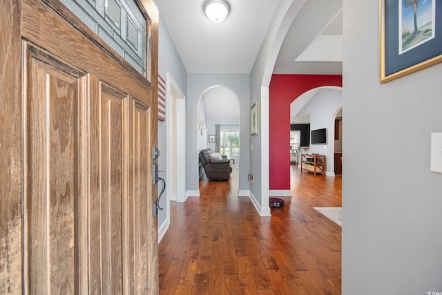 foyer with dark wood-type flooring, arched walkways, and baseboards