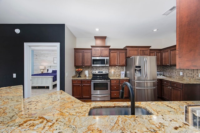 kitchen with sink, decorative backsplash, light stone counters, and stainless steel appliances