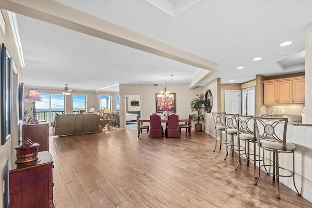 living room with light wood-type flooring, ceiling fan with notable chandelier, and a tray ceiling