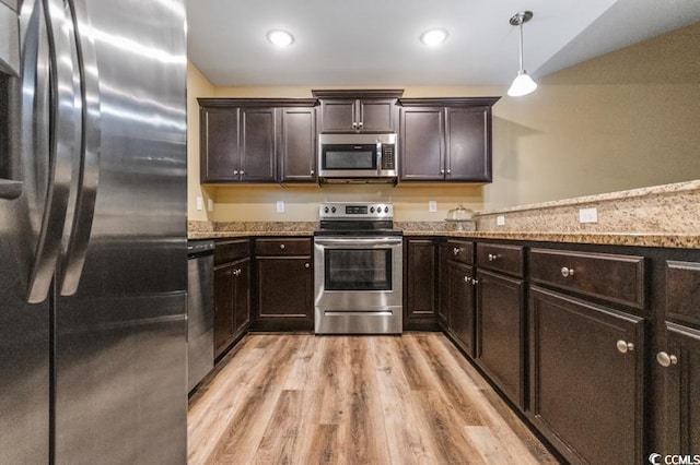 kitchen with stainless steel appliances, light stone countertops, hanging light fixtures, and light hardwood / wood-style flooring