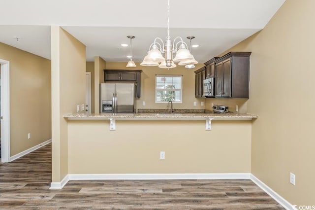 kitchen featuring dark brown cabinetry, a chandelier, pendant lighting, hardwood / wood-style flooring, and stainless steel appliances