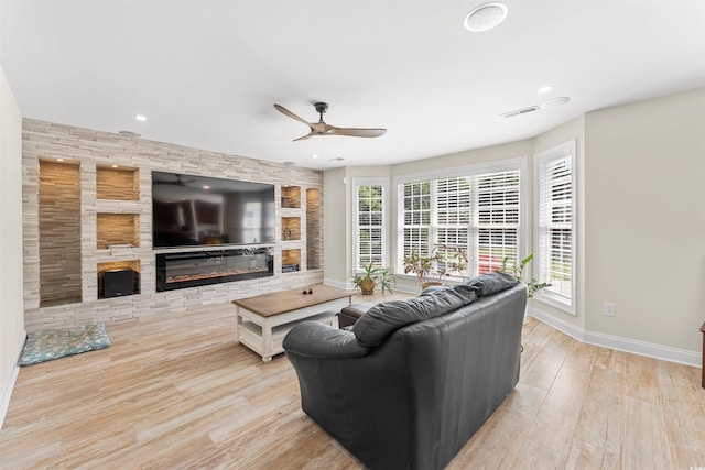 living room with a stone fireplace, ceiling fan, plenty of natural light, and light hardwood / wood-style floors