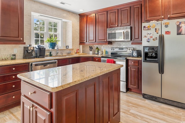 kitchen with backsplash, appliances with stainless steel finishes, and light hardwood / wood-style flooring