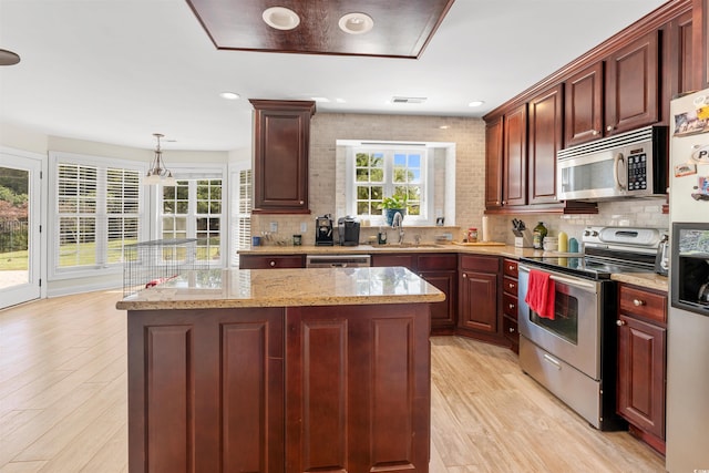 kitchen featuring decorative light fixtures, light wood-type flooring, stainless steel appliances, and a wealth of natural light