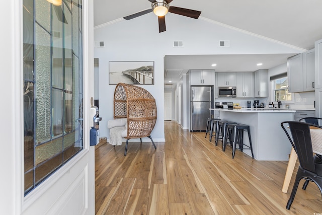 interior space featuring lofted ceiling, stainless steel appliances, a kitchen bar, and light hardwood / wood-style flooring