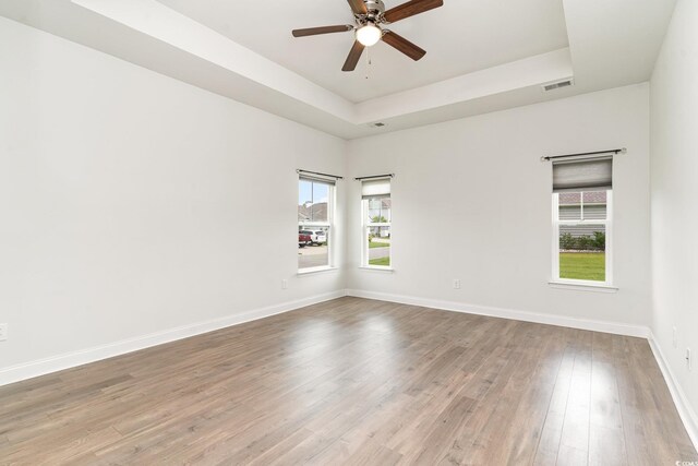 empty room with wood-type flooring, ceiling fan, and a raised ceiling