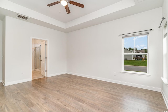 spare room featuring a raised ceiling, light wood-type flooring, and ceiling fan