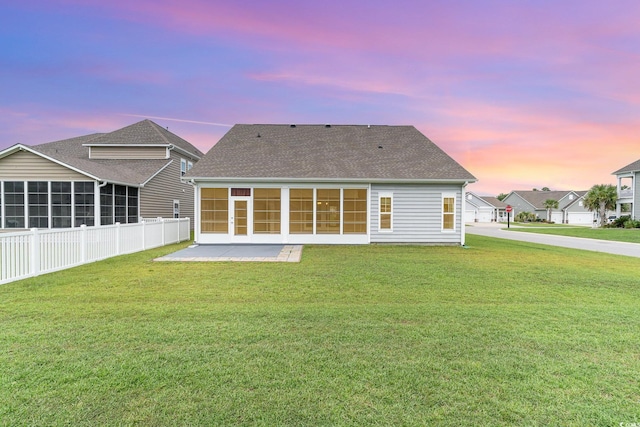 back house at dusk featuring a sunroom, a lawn, and a patio area