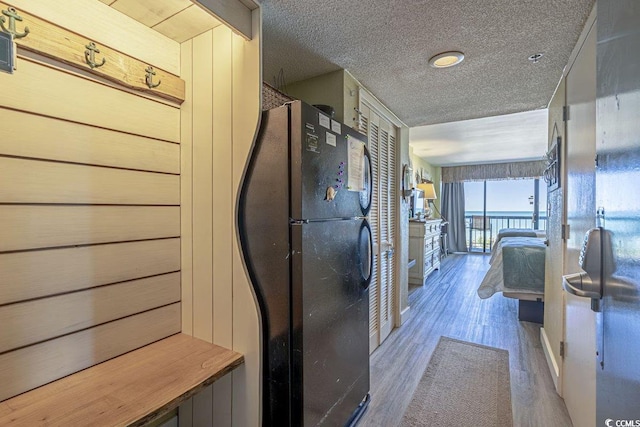 kitchen with black refrigerator, butcher block countertops, wood walls, light wood-type flooring, and a textured ceiling