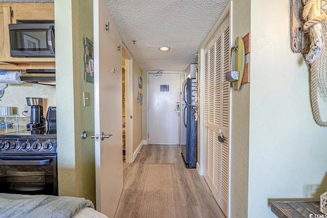 hall with light wood-type flooring and a textured ceiling