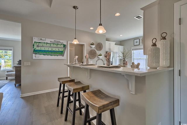 kitchen featuring hardwood / wood-style flooring, white cabinetry, stainless steel refrigerator, hanging light fixtures, and a breakfast bar area