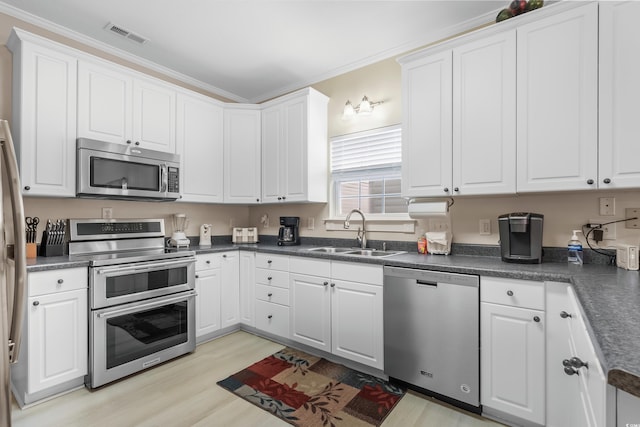 kitchen with white cabinets, crown molding, sink, light hardwood / wood-style floors, and stainless steel appliances