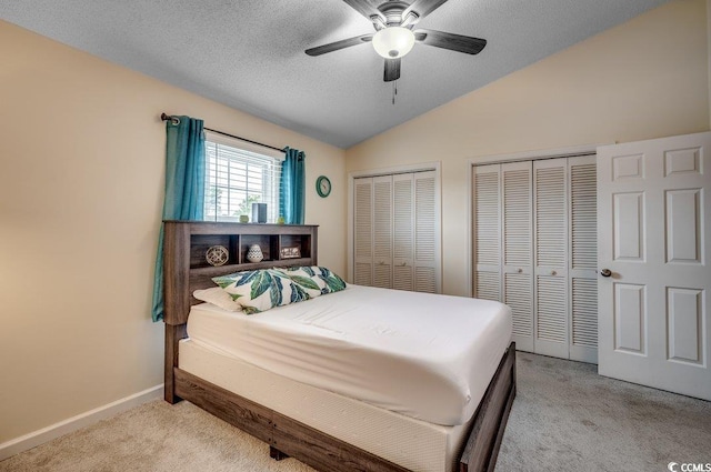 bedroom featuring vaulted ceiling, light colored carpet, a textured ceiling, two closets, and ceiling fan