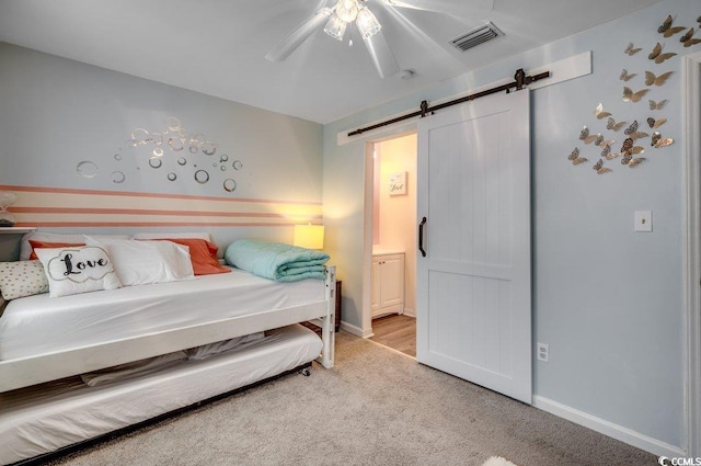 bedroom with ceiling fan, ensuite bathroom, a barn door, and light carpet