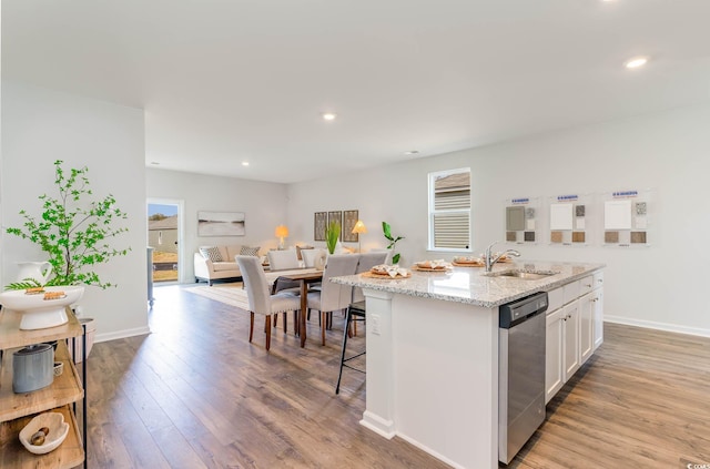 kitchen featuring stainless steel dishwasher, a kitchen island with sink, sink, light hardwood / wood-style flooring, and white cabinets