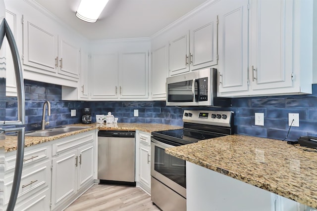 kitchen featuring a sink, stainless steel appliances, light wood-style flooring, backsplash, and white cabinetry