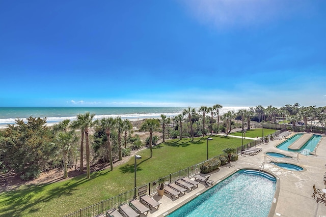 community pool featuring a yard, a beach view, a patio, a water view, and fence