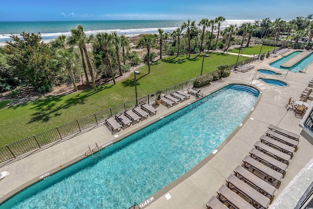 community pool featuring a patio, a yard, a water view, and fence