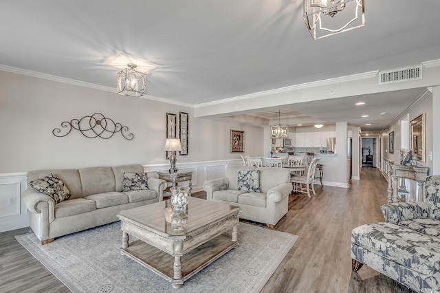 living area with a chandelier, ornamental molding, light wood-type flooring, and visible vents