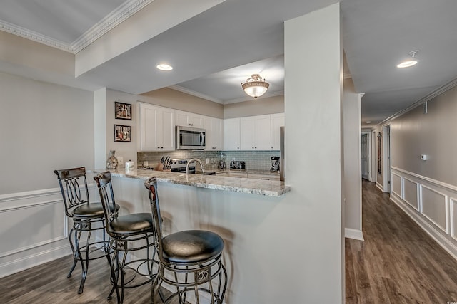 kitchen with white cabinets, ornamental molding, appliances with stainless steel finishes, decorative backsplash, and dark wood-style floors