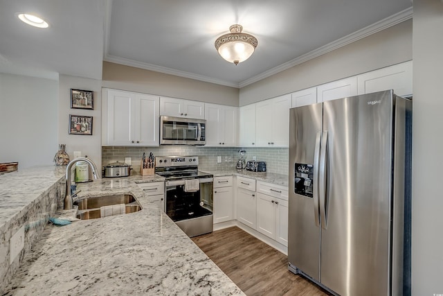 kitchen with stainless steel appliances, tasteful backsplash, ornamental molding, a sink, and wood finished floors