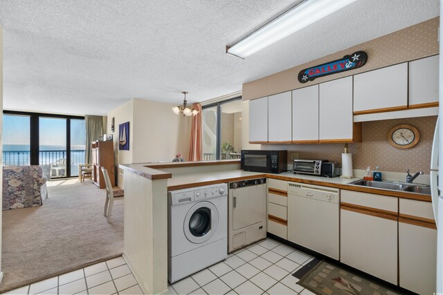 kitchen featuring washer / clothes dryer, sink, white cabinets, white dishwasher, and a water view