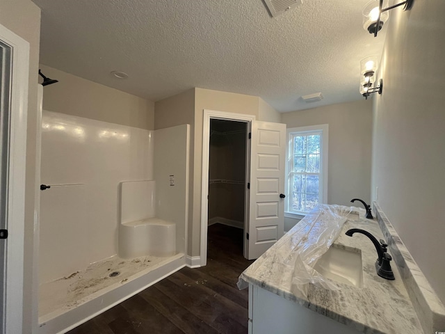 bathroom featuring vanity, wood-type flooring, a shower, and a textured ceiling