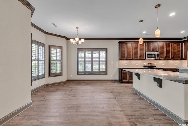 kitchen featuring a kitchen breakfast bar, stainless steel appliances, dark brown cabinets, decorative light fixtures, and light stone counters