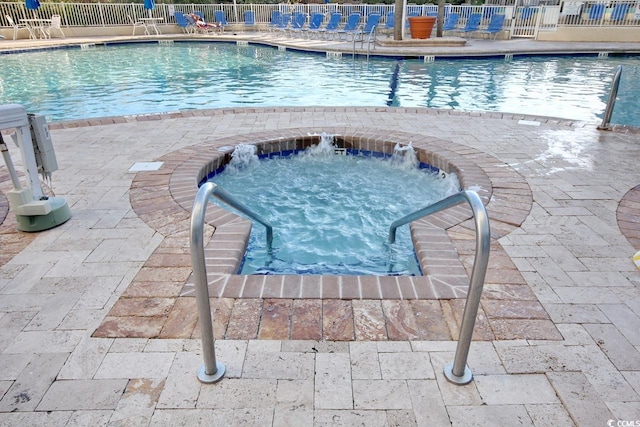 pool with fence, a hot tub, and a patio