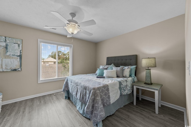 bedroom with a textured ceiling, wood-type flooring, and ceiling fan