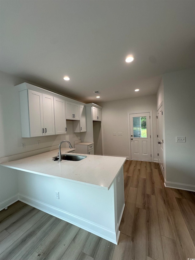 kitchen featuring kitchen peninsula, sink, hardwood / wood-style flooring, and white cabinets