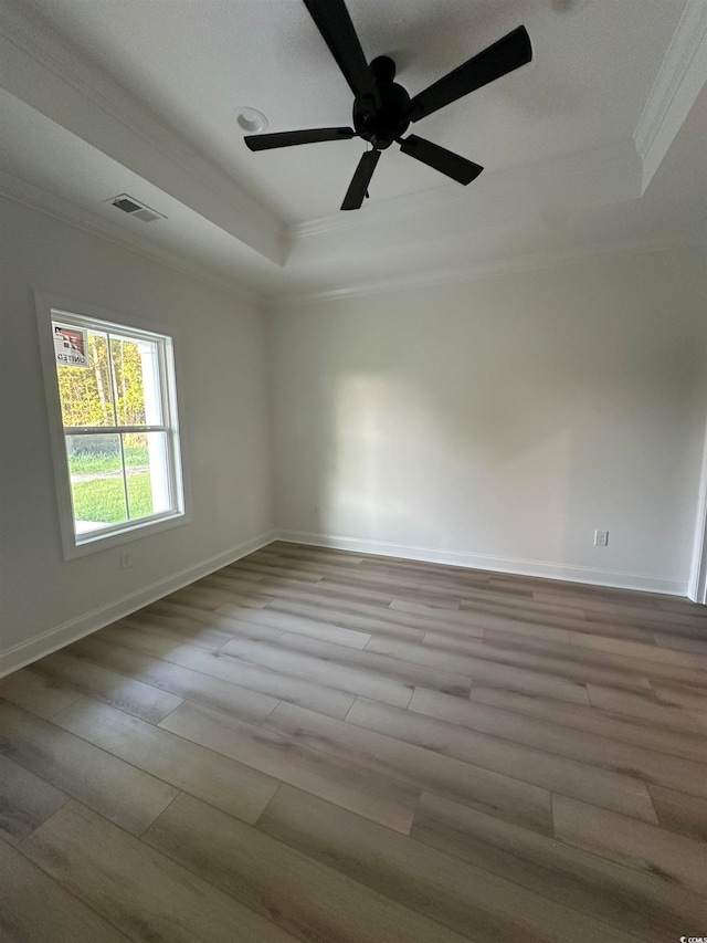 empty room featuring ceiling fan, a raised ceiling, light wood-type flooring, and crown molding