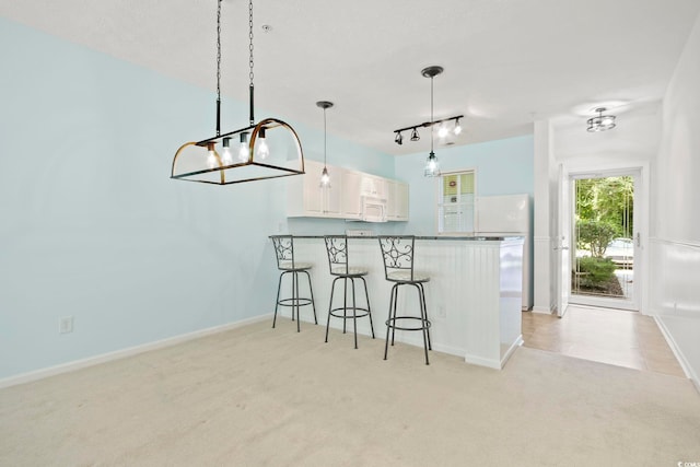 kitchen with light colored carpet, a breakfast bar area, decorative light fixtures, kitchen peninsula, and white cabinets