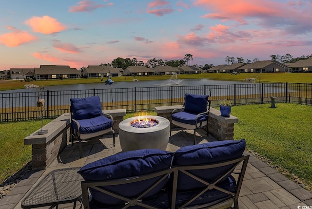 patio terrace at dusk with a water view, a yard, and a fire pit