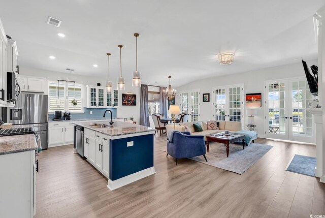 kitchen featuring appliances with stainless steel finishes, an island with sink, hanging light fixtures, light stone counters, and french doors