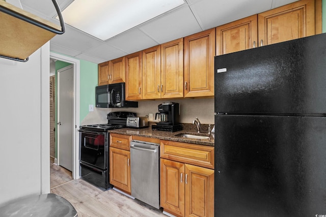 kitchen featuring a drop ceiling, light wood-style flooring, brown cabinetry, black appliances, and a sink