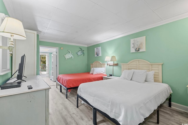 bedroom featuring light wood finished floors, baseboards, and ornamental molding