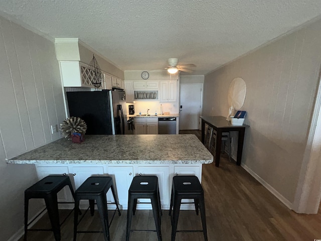 kitchen featuring a breakfast bar area, white cabinetry, black fridge, stainless steel dishwasher, and kitchen peninsula