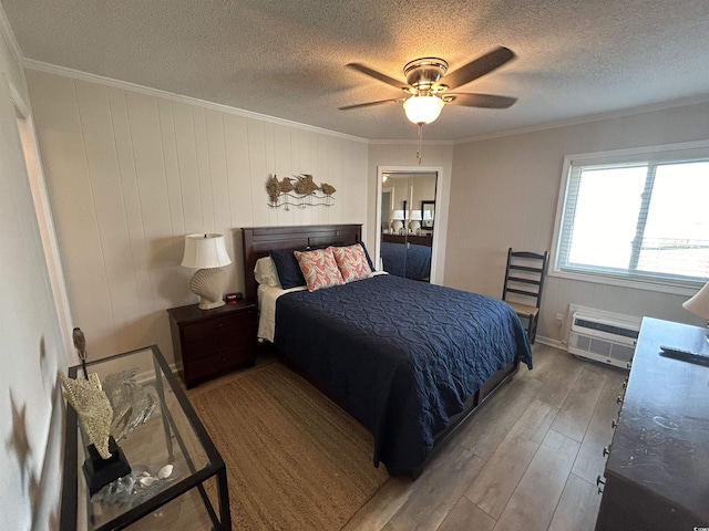 bedroom featuring ceiling fan, hardwood / wood-style floors, ornamental molding, a textured ceiling, and an AC wall unit